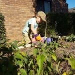 boy in garden watering plants with an orange watering can