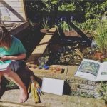 child sitting on the edge of a homemade wildlife pond in the garden drawing