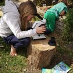 children in the garden - one looking into pond, one with microscope