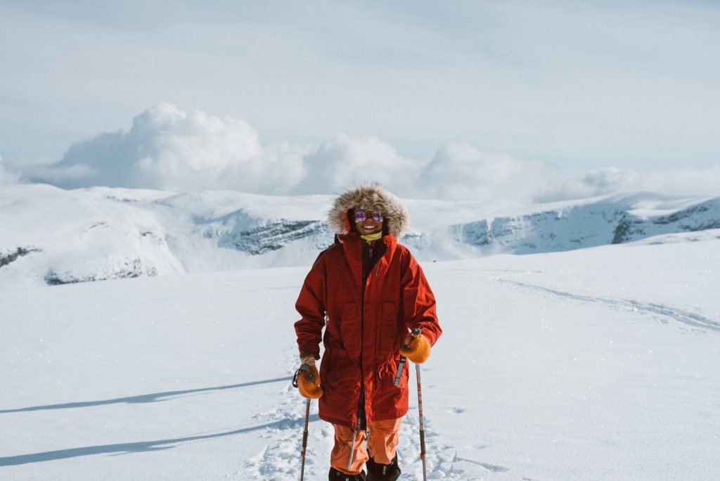person in a red hooded coat in a snowy scene smiling with walking poles
