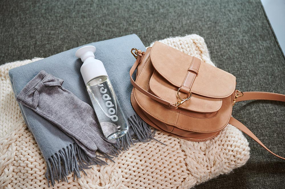 dopper glass bottle next to a brown satchel on a folded scarf