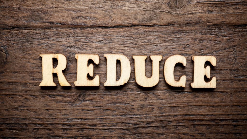 The word "reduce" on a wooden background, indicating reducing our overconsumption of resources